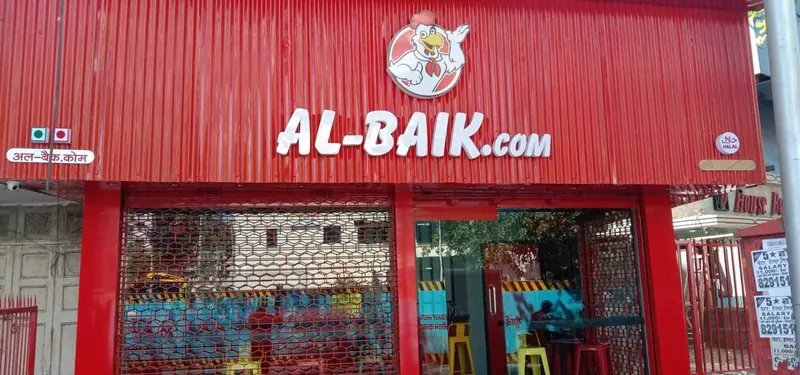 AL-BAIK.COM storefront with red cladding and chicken mascot sign, Bharuch, India