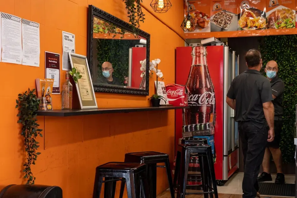 Inside Big Charcoal Chicken with bar stools, a drinks fridge and the menu board