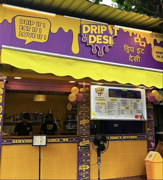 Drip It Desi café counter with purple and yellow drip signage and menu board, Mumbai, India